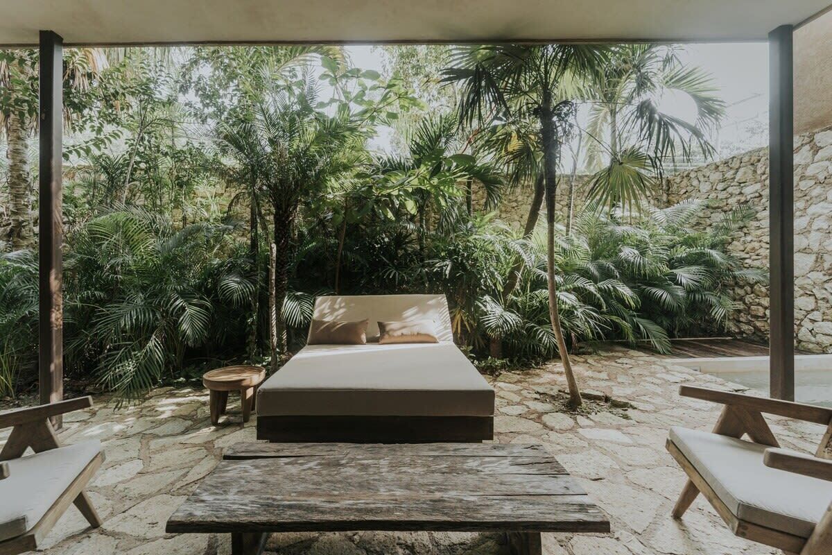 A bed with a beige mattress and pillows, surrounded by a stone floor and wooden furniture.