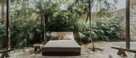 A bed with a beige mattress and pillows, surrounded by a stone floor and wooden furniture.