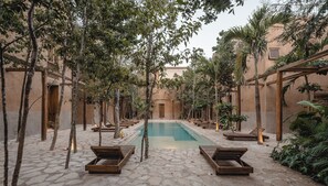 A courtyard with a pool, wooden loungers, and trees.