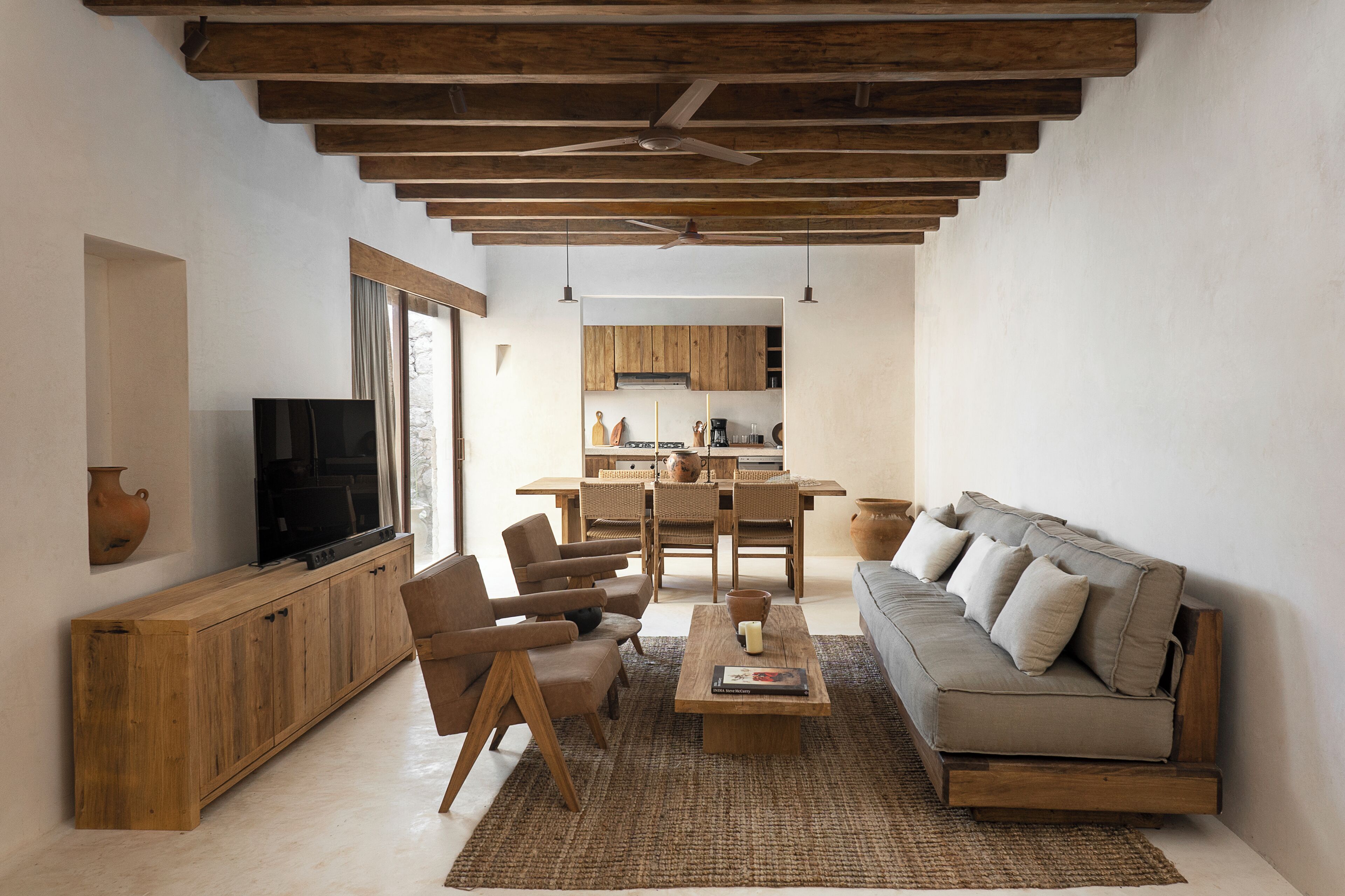 A spacious living room with a wooden ceiling, a sofa, a coffee table, and a TV on a wooden cabinet.