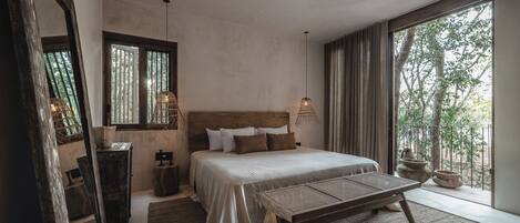 Un dormitorio con una cama grande, un banco de madera, un espejo y vistas a árboles por la ventana.