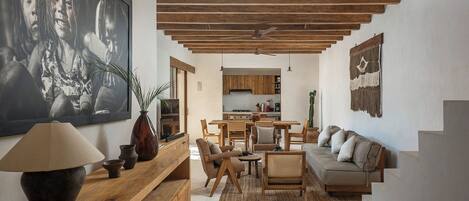 A spacious living area with a wooden ceiling, a sofa, a dining table, and a kitchen in the background.