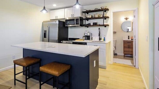 Una cocina moderna con una isla central, taburetes de bar, microondas y un lavabo.