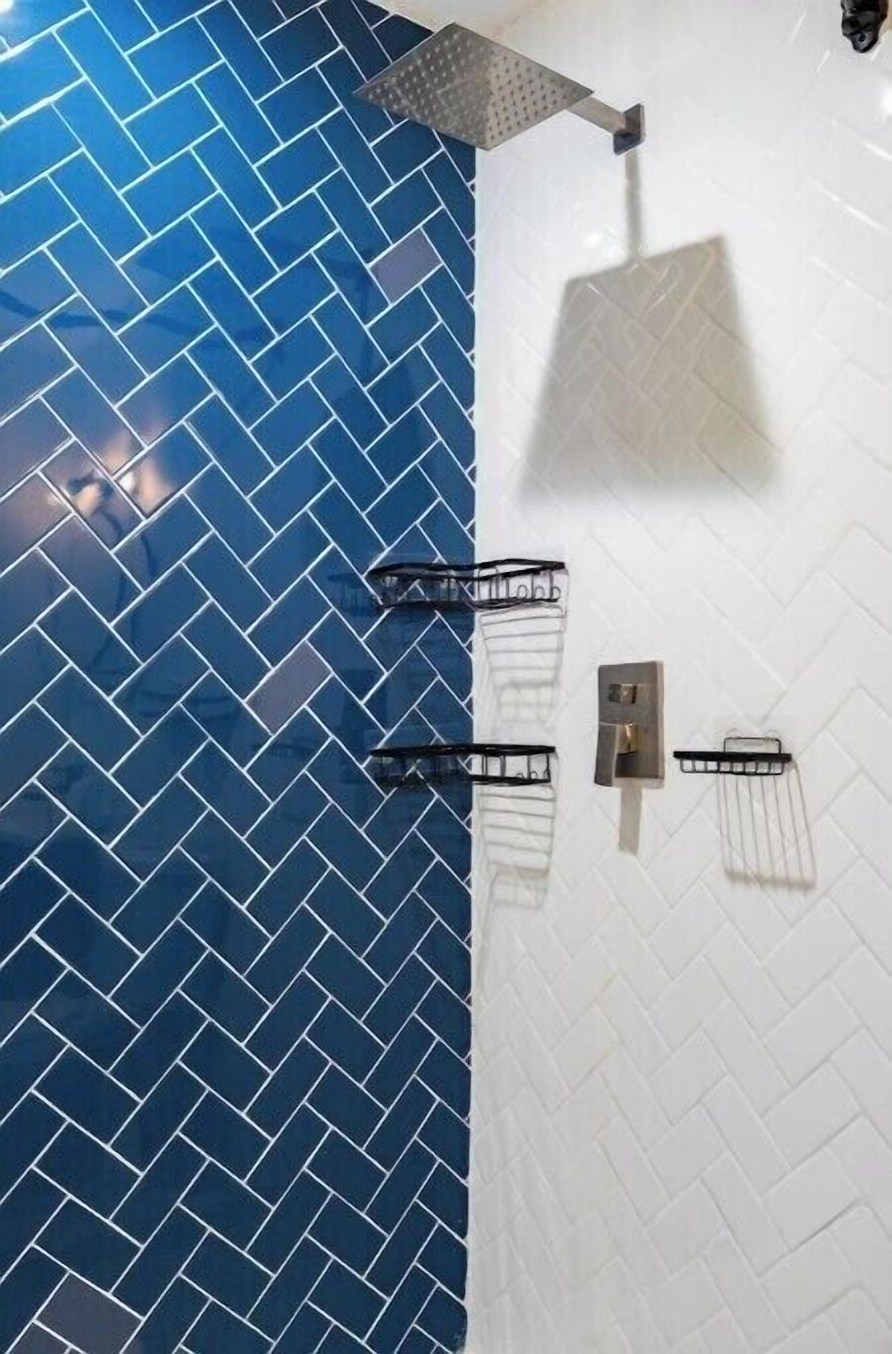 A bathroom with a blue and white herringbone tile pattern, a showerhead, and two towel racks.