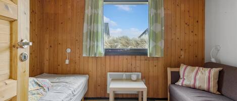 Una habitación pequeña y acogedora con paredes de madera, una ventana con cortinas, una cama, una mesa y un sofá.