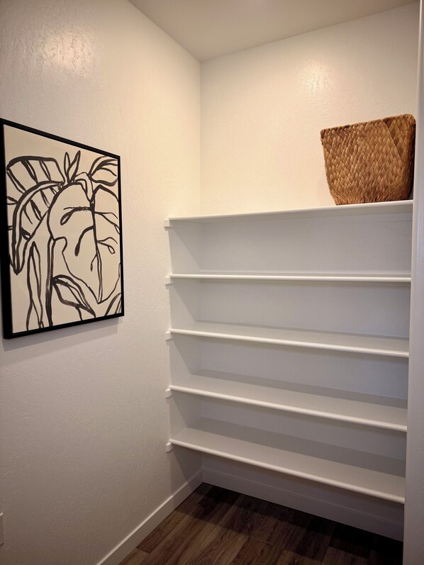 A hallway with white walls, a wooden floor, and a white shelf unit with a woven basket on top.