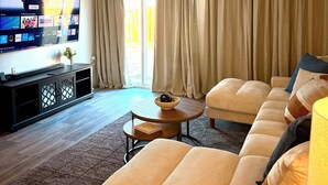 A living room with a flat-screen TV, beige curtains, a sofa, and a coffee table. - Newly built, stylish 3BR/2BA home in a quiet Bakersfield neighborhood. (Bakersfield)