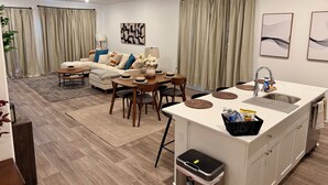 A modern living room with a sofa, coffee table, and dining area. There is a kitchen with a sink and cabinets. - Newly built, stylish 3BR/2BA home in a quiet Bakersfield neighborhood. (Bakersfield)