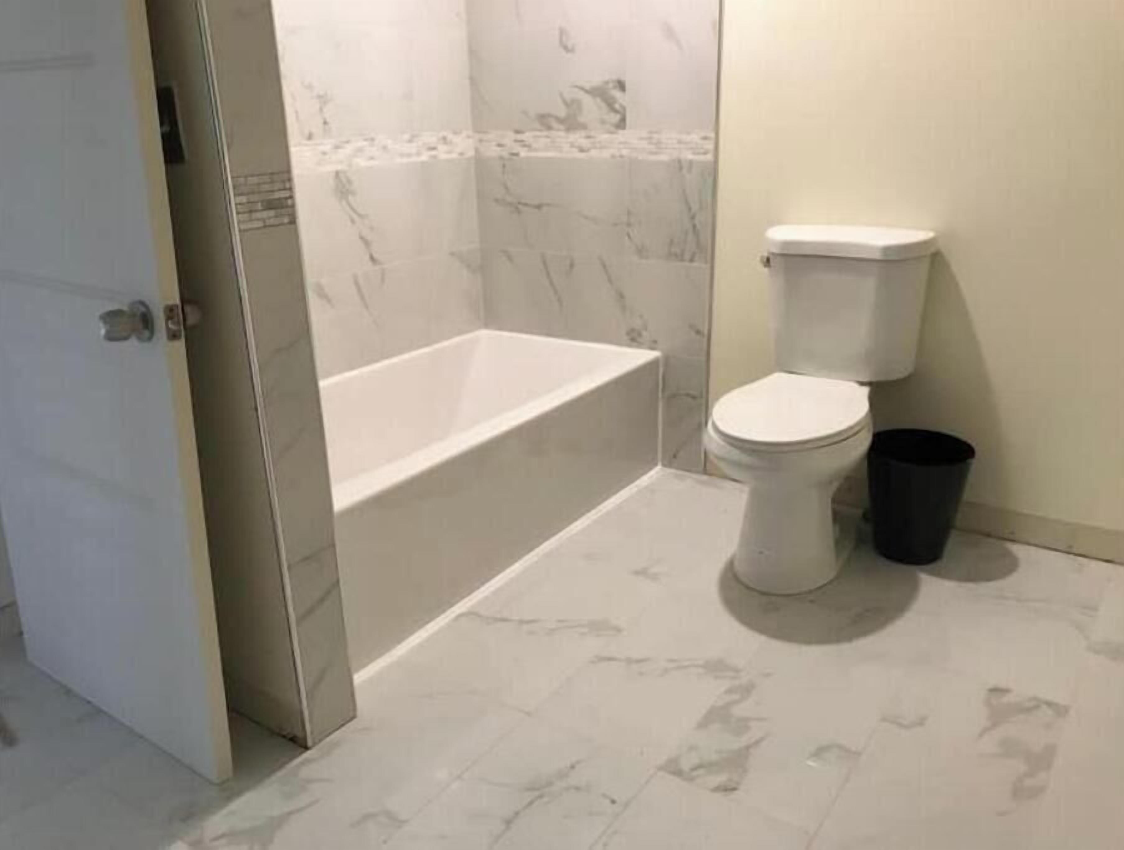 A bathroom with a bathtub, toilet, and a trash bin.