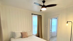 Ein Schlafzimmer mit einem Bett, einem Deckenventilator, einer Stehlampe und einer Tür zu einem anderen Raum.