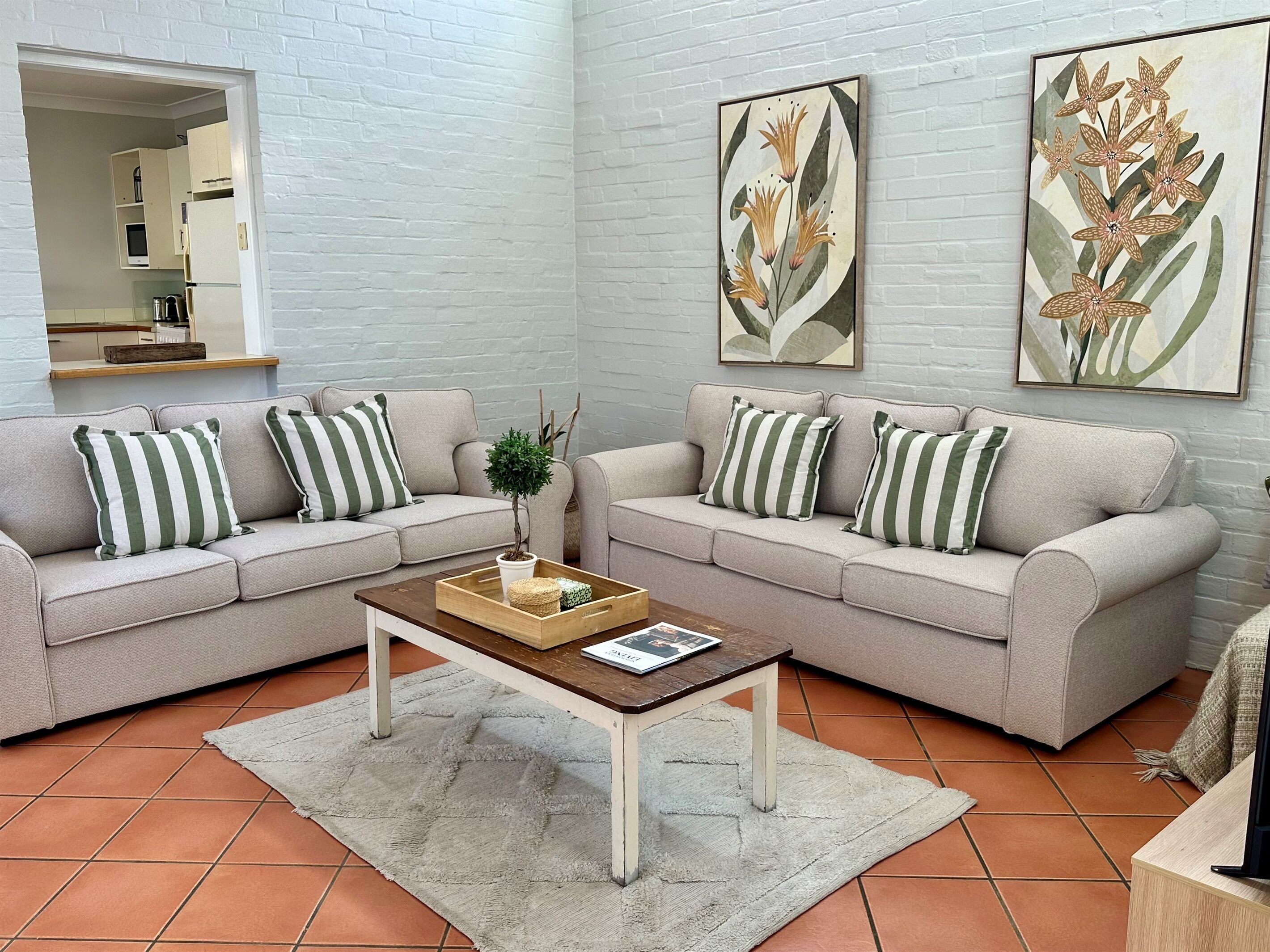 Ein Wohnzimmer mit zwei Sofas, einem Couchtisch und einer kleinen Pflanze. An der Wand befinden sich zwei gerahmte Blumenbilder.