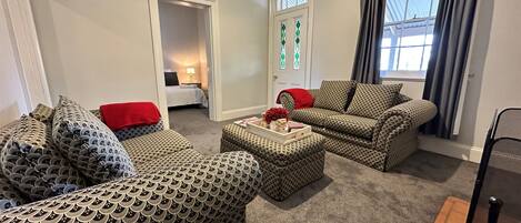 A living room with patterned sofas, a coffee table with decorative items, and a view of a bedroom through an open door.