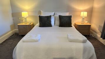 A neatly made bed with white linens, two bedside tables with lamps, and a plain wall.