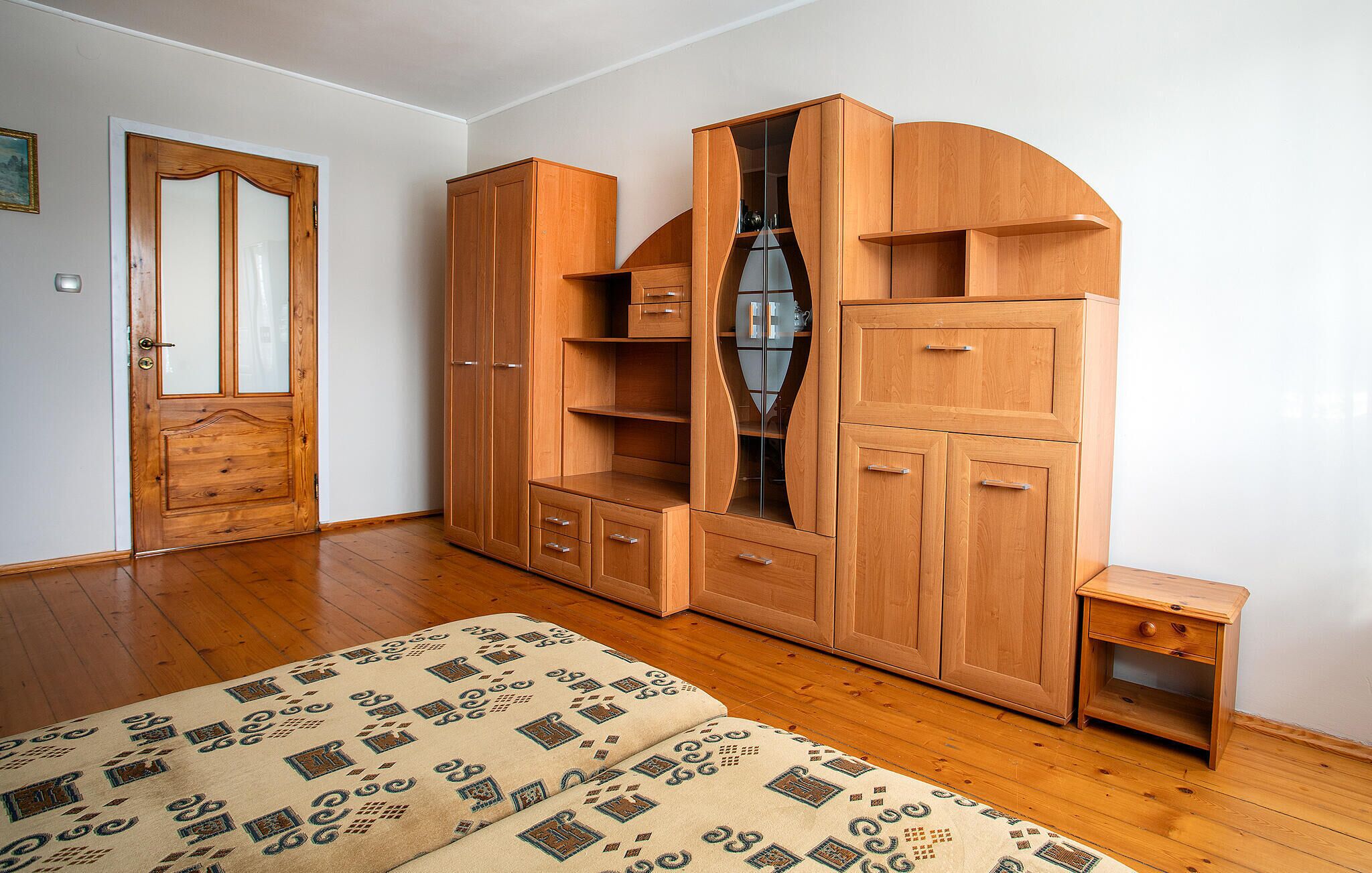Un dormitorio con un armario de madera, una cama con ropa de cama estampada y una mesita de noche pequeña.