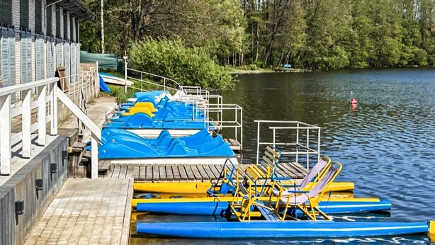 A dock with paddle boats and lounge chairs by a calm lake, surrounded by trees.