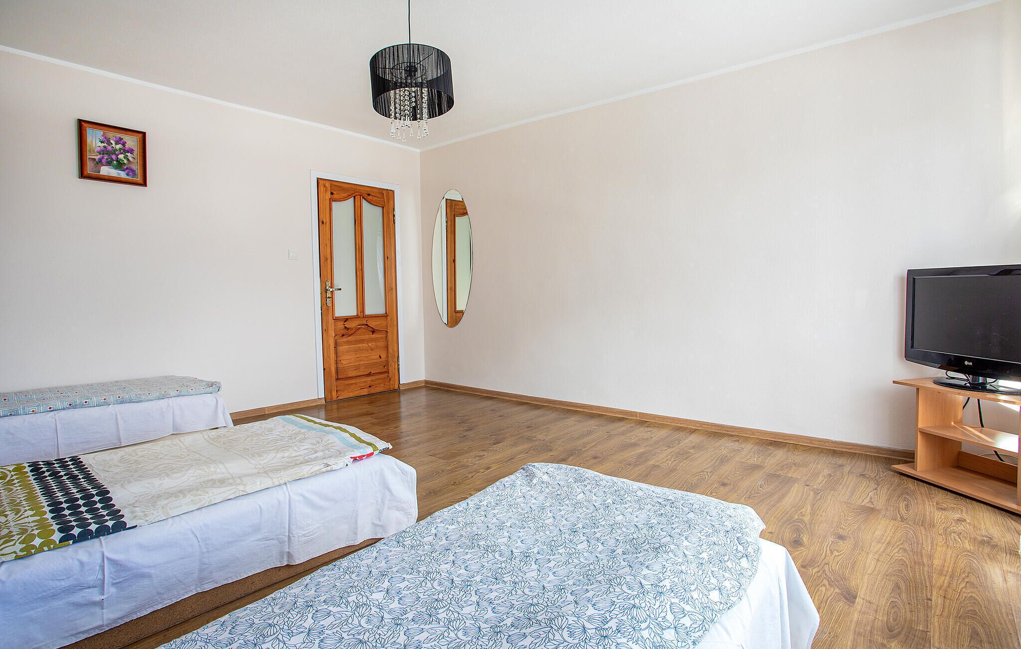 Une chambre avec deux lits, un plancher en bois, un téléviseur posé sur un meuble en bois, une porte avec un miroir et un luminaire suspendu.