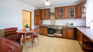 A kitchen with wooden cabinets, a stove, an oven, a microwave, and a dining area with chairs and a table.
