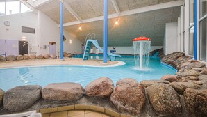 Une piscine intérieure avec un toboggan, des éléments décoratifs en forme de rochers et une horloge au mur.