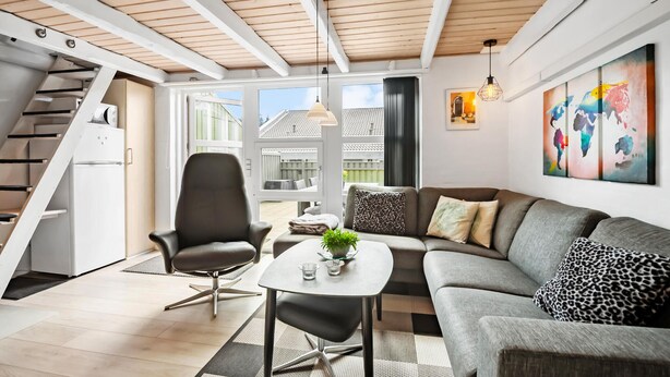 Un salon moderne comprenant un canapé, un fauteuil et une table basse, un escalier et une grande fenêtre donnant sur l’extérieur.