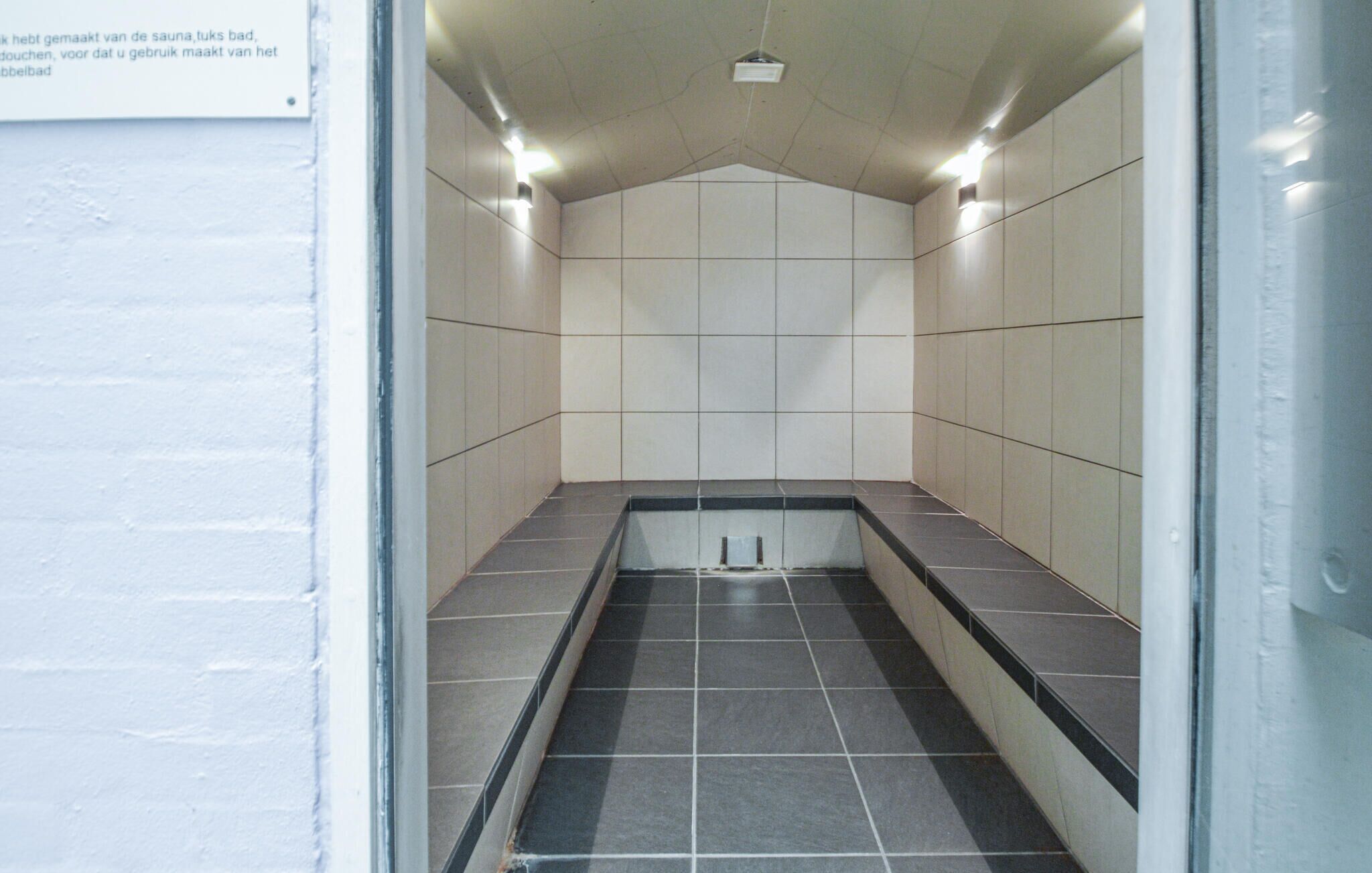Un sauna carrelé, avec un banc et un luminaire au plafond.