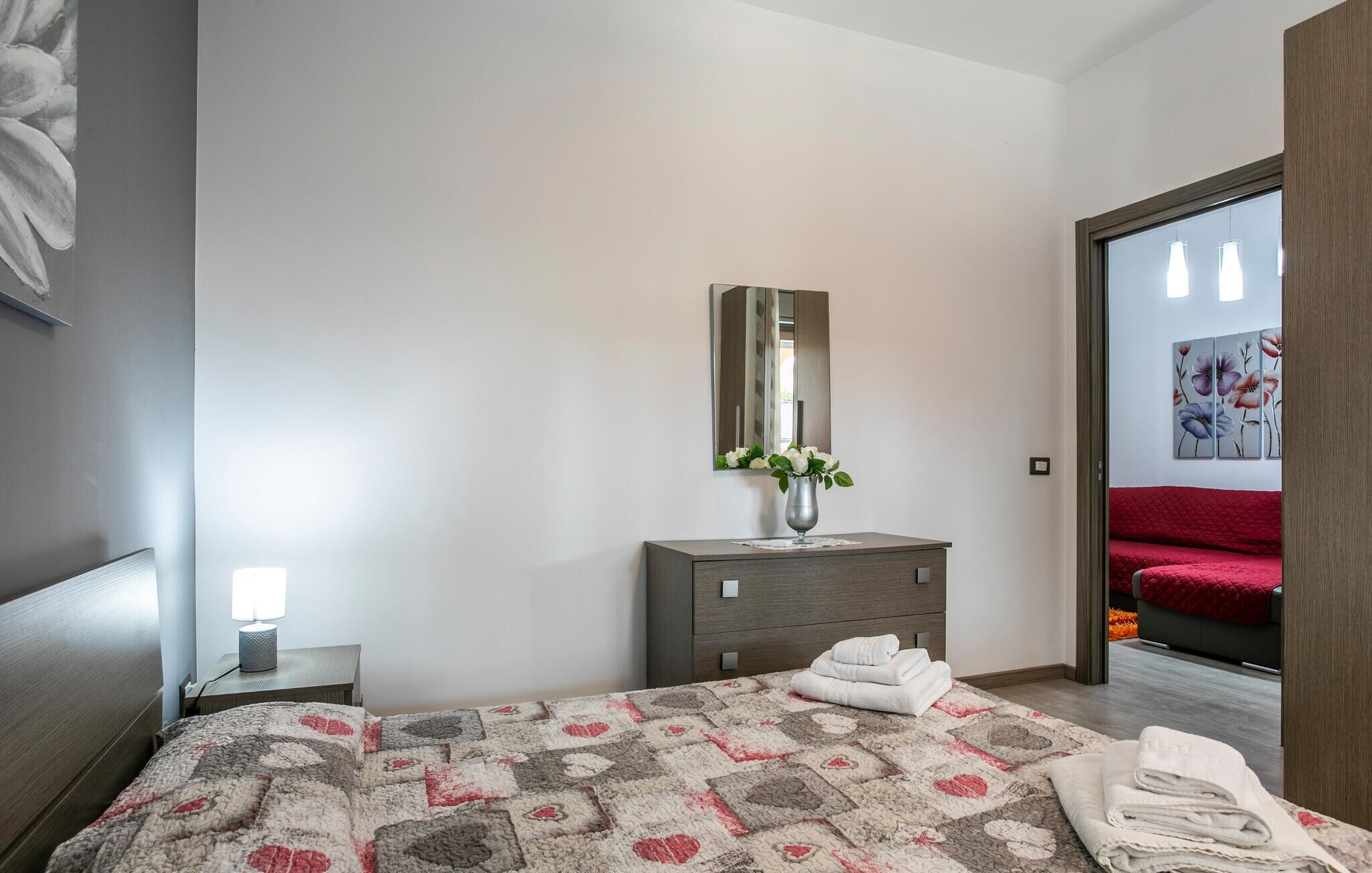 A modern bedroom with a bed, a dresser, a mirror, and a vase with flowers.