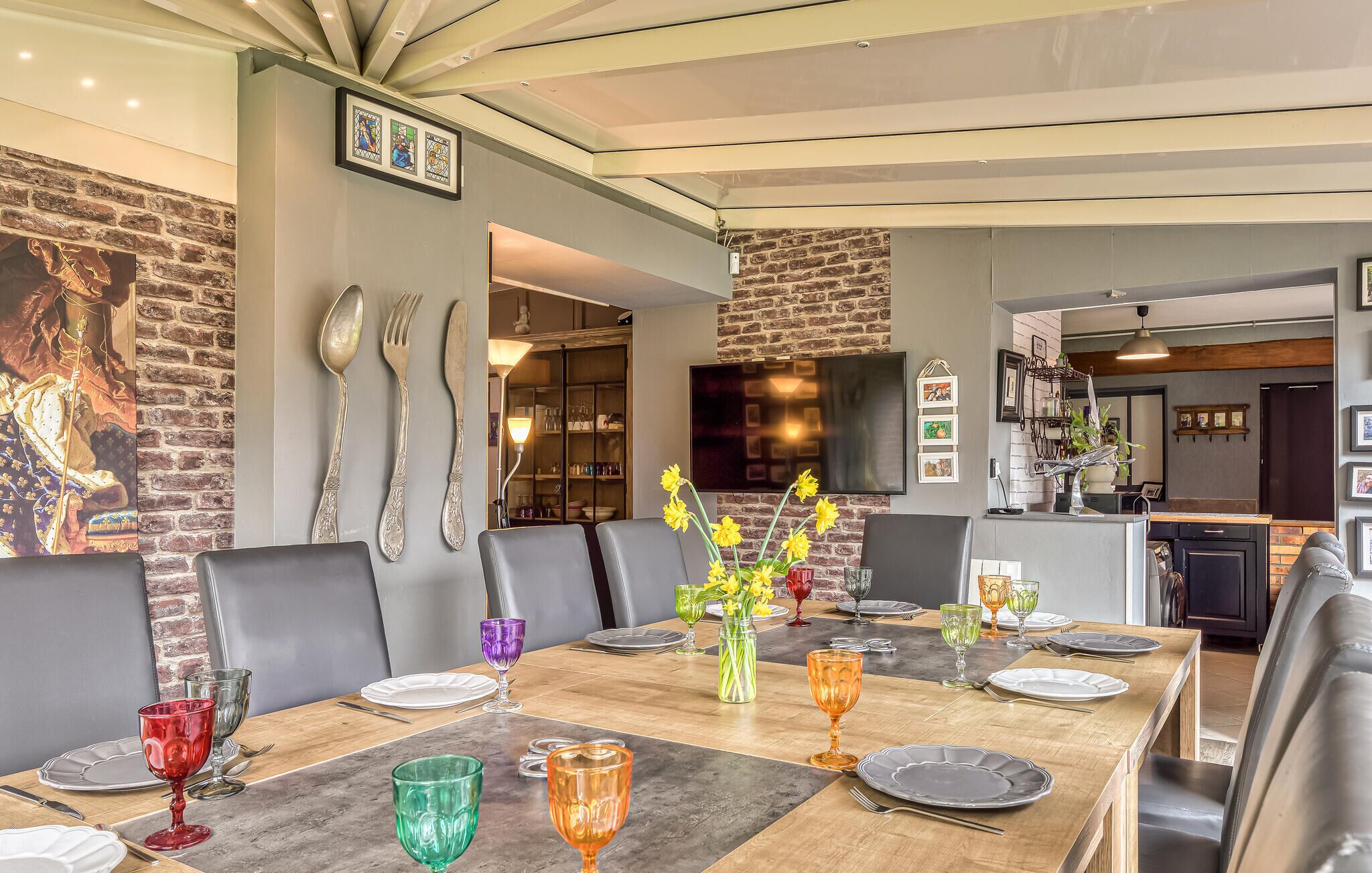 A dining area with a brick wall, a large painting, and a modern kitchen in the background.