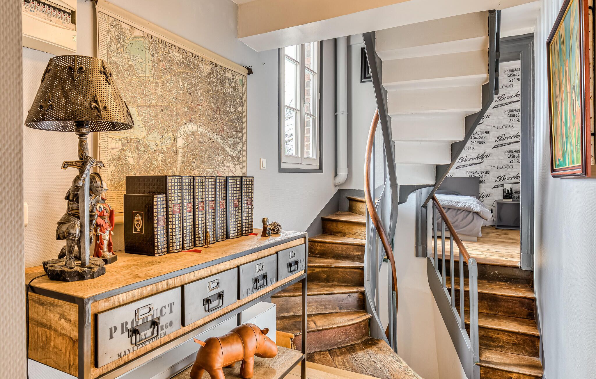 A staircase with a metal railing, a wooden desk with drawers, a map on the wall, and a lamp.