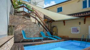 A swimming pool with two blue lounge chairs, a stone wall, and a wooden deck. - Lovely apartment in Veli Brgud with WiFi (Veli Brgud)