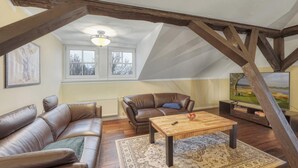 Un salon de style industriel, avec des poutres en bois apparentes, un canapé en cuir marron, une table basse en bois et une grande fenêtre donnant sur la forêt.