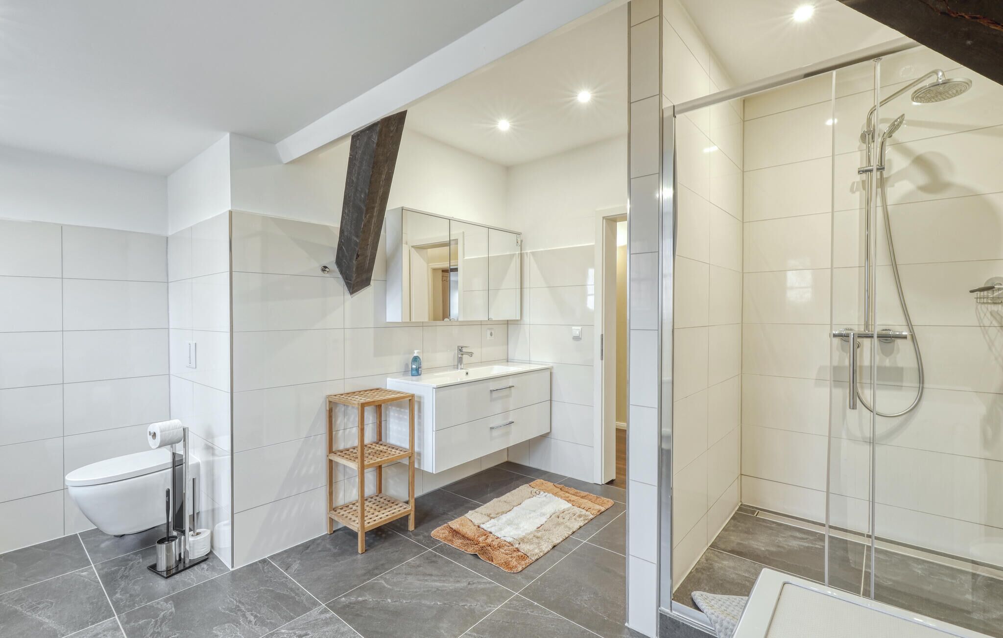A modern bathroom with a glass shower enclosure, a white sink, and a wooden vanity.