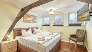 Une chambre à coucher comprenant un lit, des tables de chevet, une chaise et un téléviseur fixé au mur.