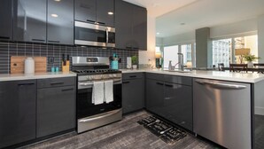 A modern kitchen with dark cabinets, stainless steel appliances, and a large window providing natural light. - City Skyline Views 3Bed Apt with Rooftop Pool, Spa,& Rooftop deck (Los Angeles)