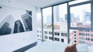 A modern hotel room with a large bed, a city view, and a wall-mounted artwork. - City Skyline Views 3Bed Apt with Rooftop Pool, Spa,& Rooftop deck (Los Angeles)