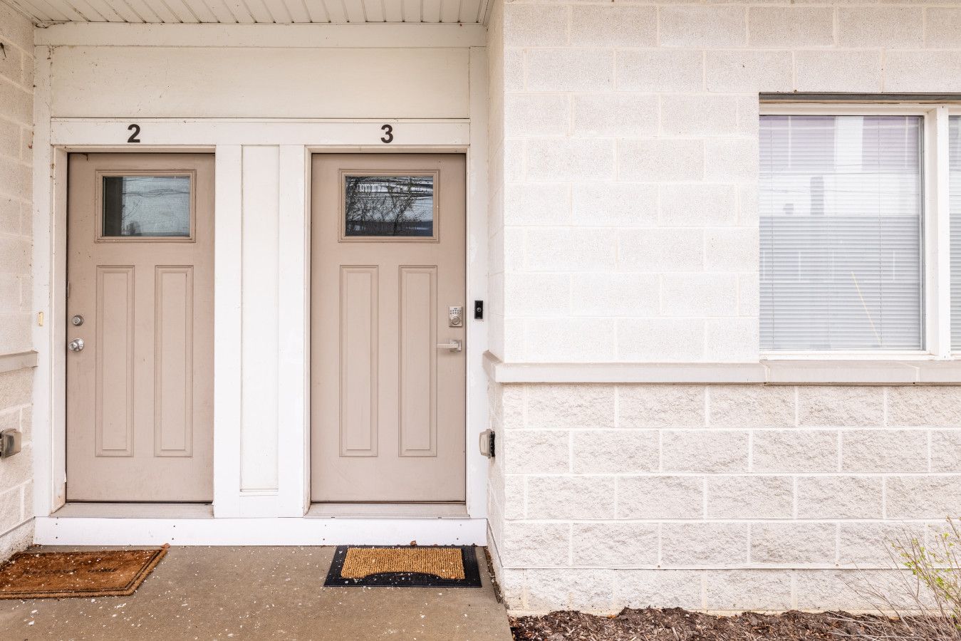 A building with two doors labeled 2 and 3, a window with blinds, and a concrete entrance with a doormat.