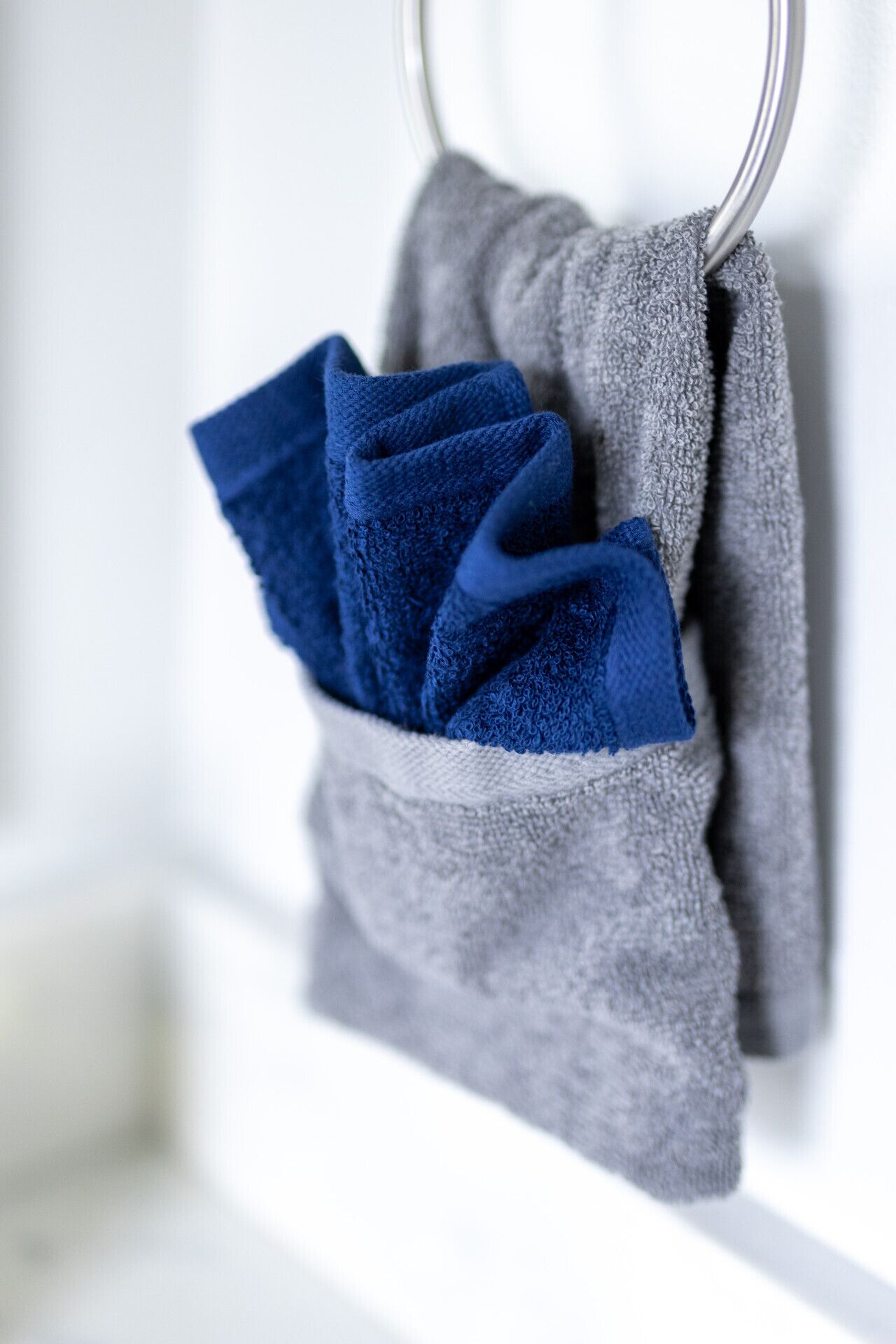 Un perchero con dos toallas, una azul y otra gris, colgadas en una pared blanca.