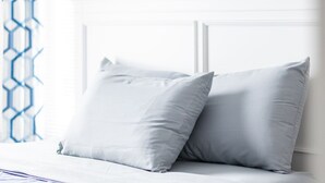 Una cama bien hecha con cabecera blanca y dos almohadas, una manta azul y una colcha estampada.