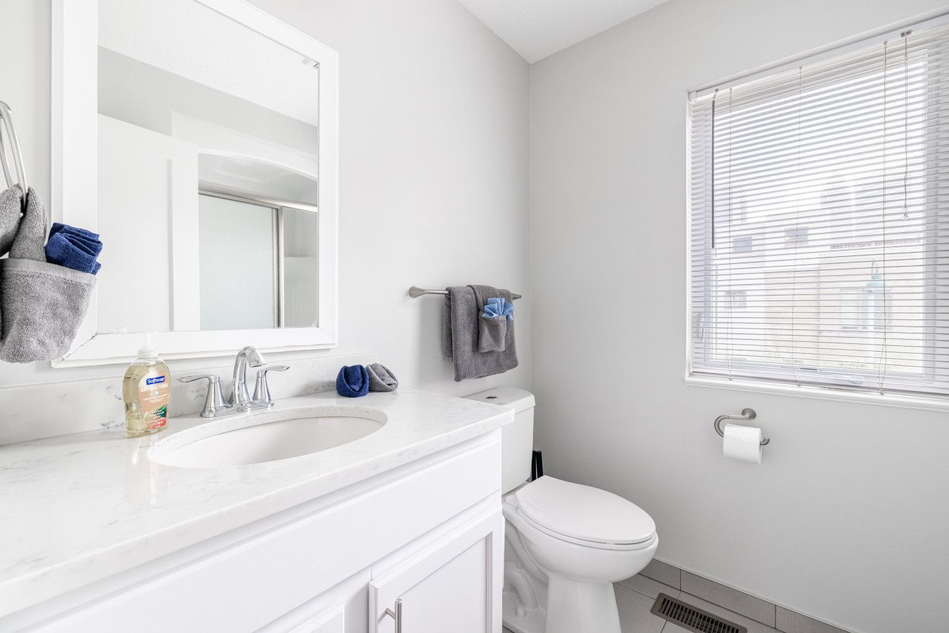 A bathroom with a white sink, mirror, and toilet. There are towels and a bottle of hand soap on the counter.
