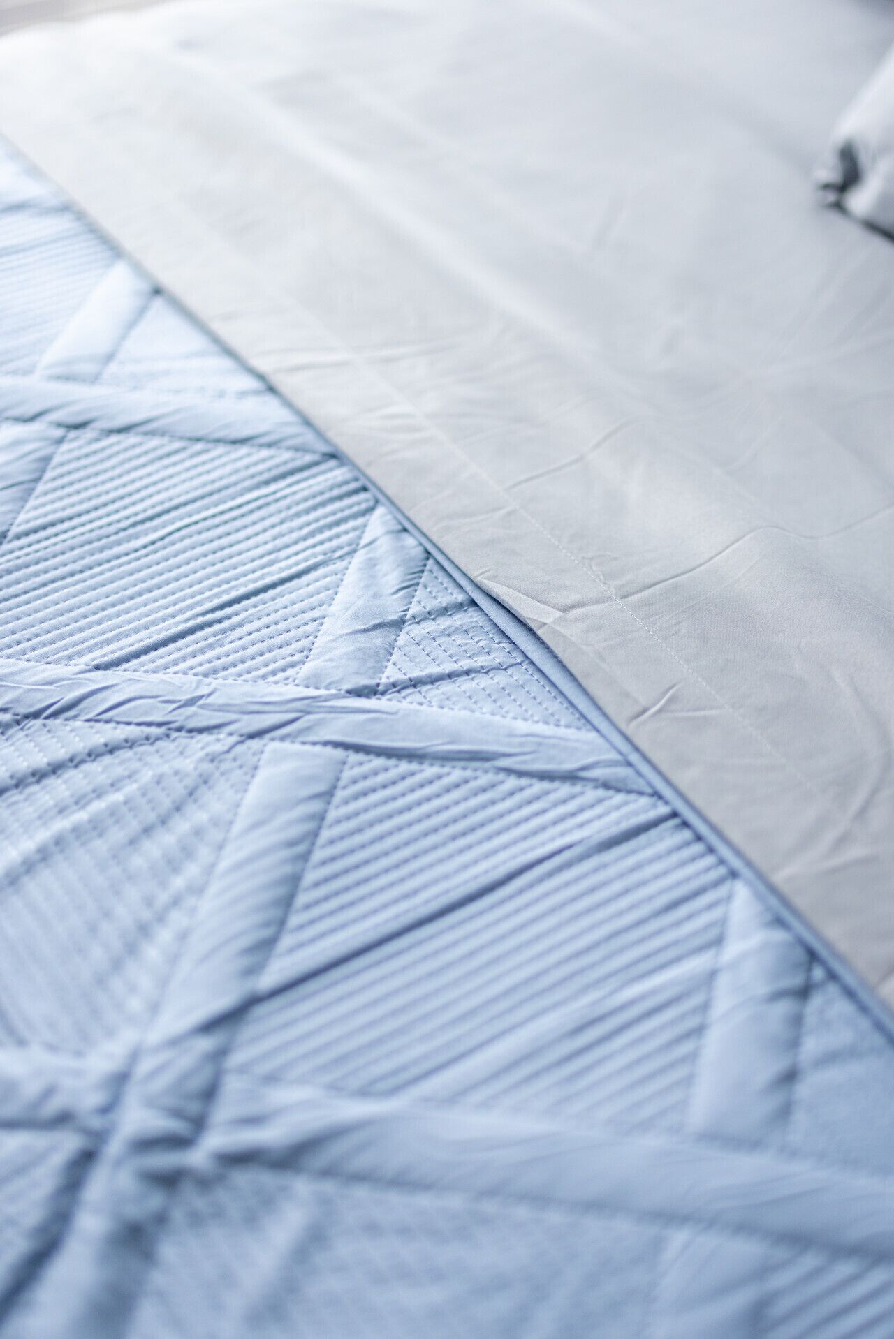 Een detail van een bed met een gewatteerd hoofdbord en een effen matras.
