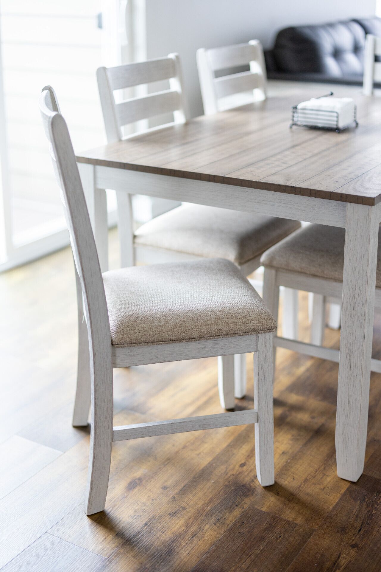 A dining table with four chairs, a candle, and a window in the background.