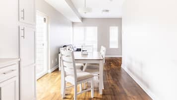 Un comedor con una mesa de madera y sillas blancas, un armario blanco y una ventana con persianas.