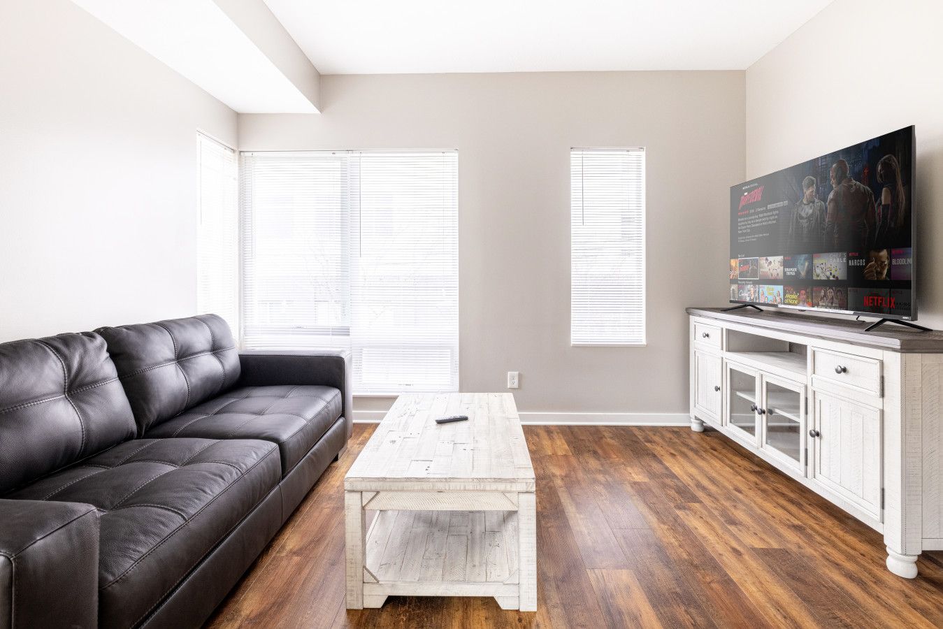 A living room with a black leather sofa, a white coffee table, and a TV on a white cabinet.