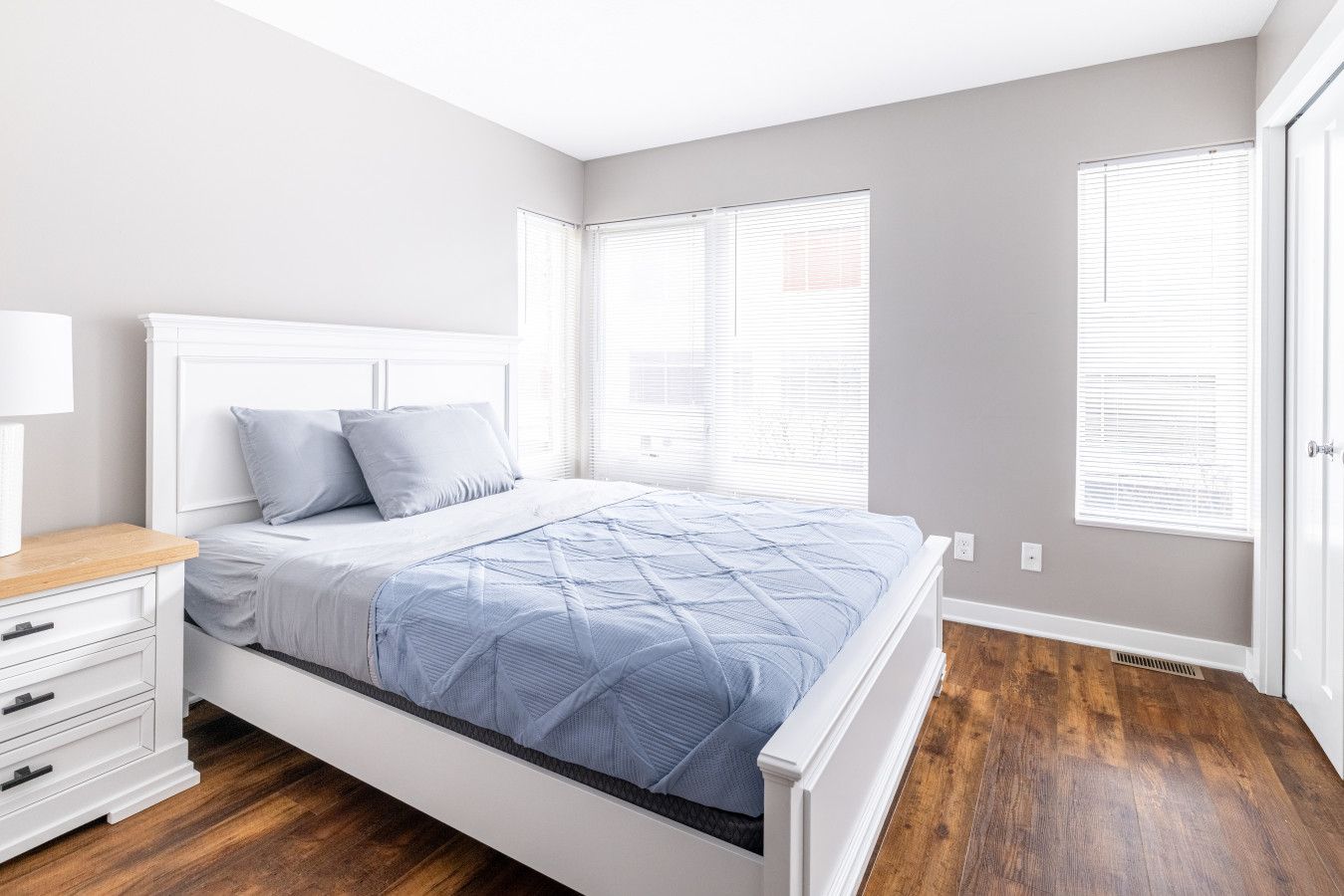 Un dormitorio con una cama, una mesita de noche y un ventanal con persianas.