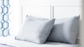 Un lit bien fait, avec une tête de lit blanche et deux oreillers, une couverture bleue et une couvre-lit à motifs.