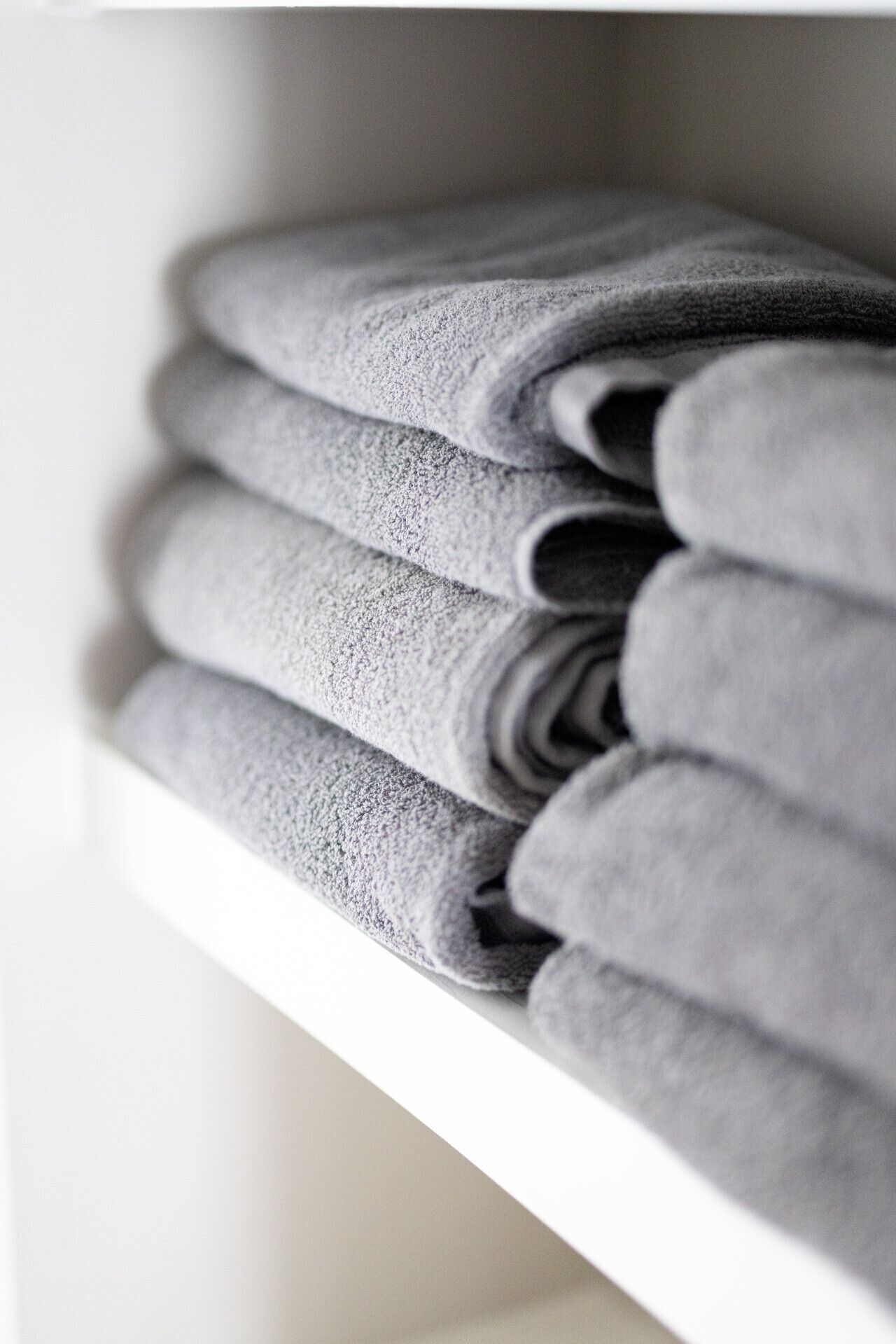 A neatly folded stack of grey towels on a white shelf.