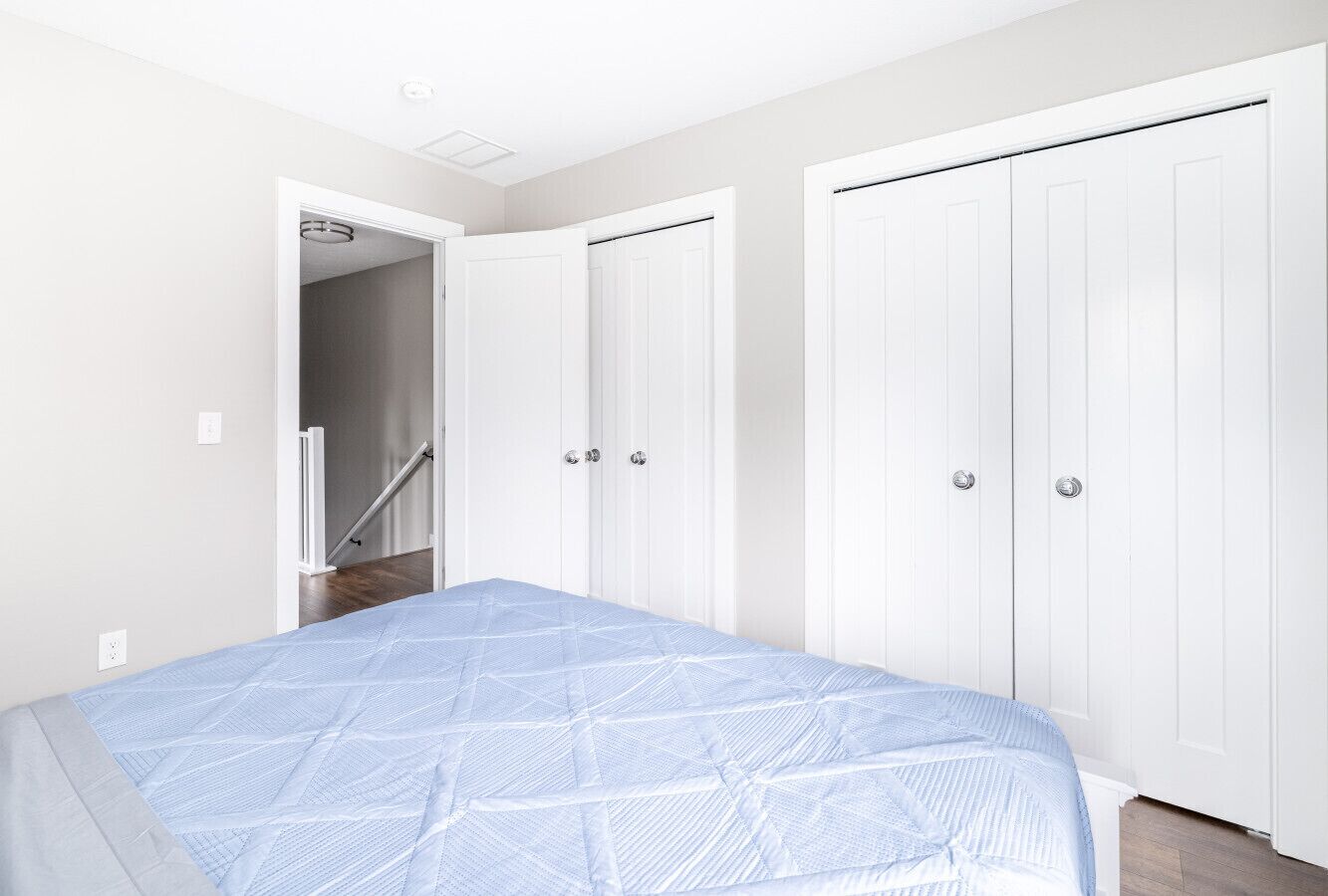 A bedroom with a bed, a white wardrobe, and a door leading to a staircase.