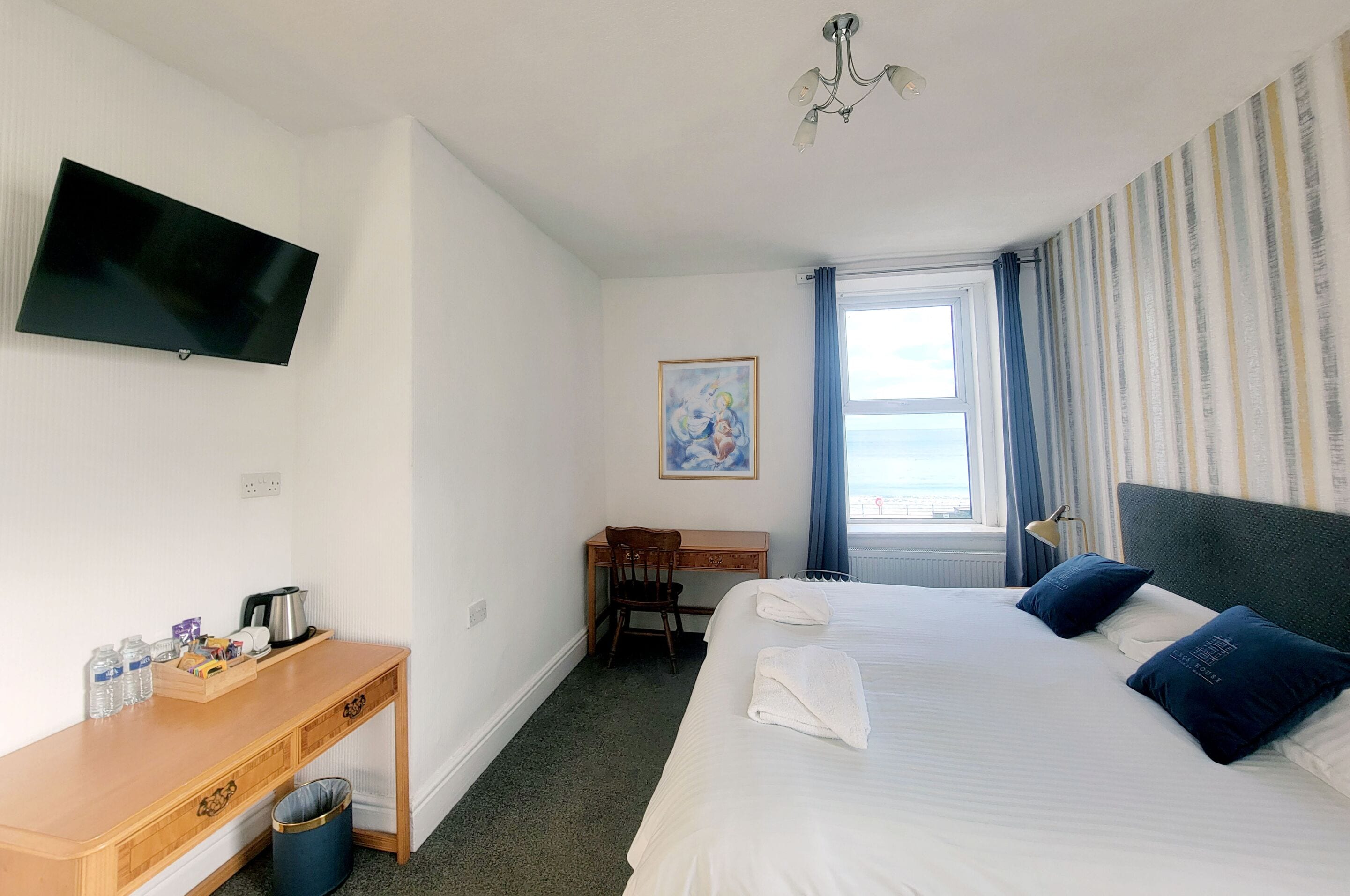 A hotel room with a bed, a desk, a chair, a television, a painting, and a window with curtains.