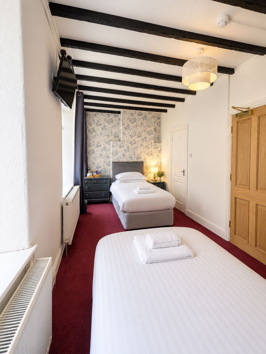 Una habitación de hotel con dos camas, un radiador, una puerta de madera y un techo con vigas a la vista.