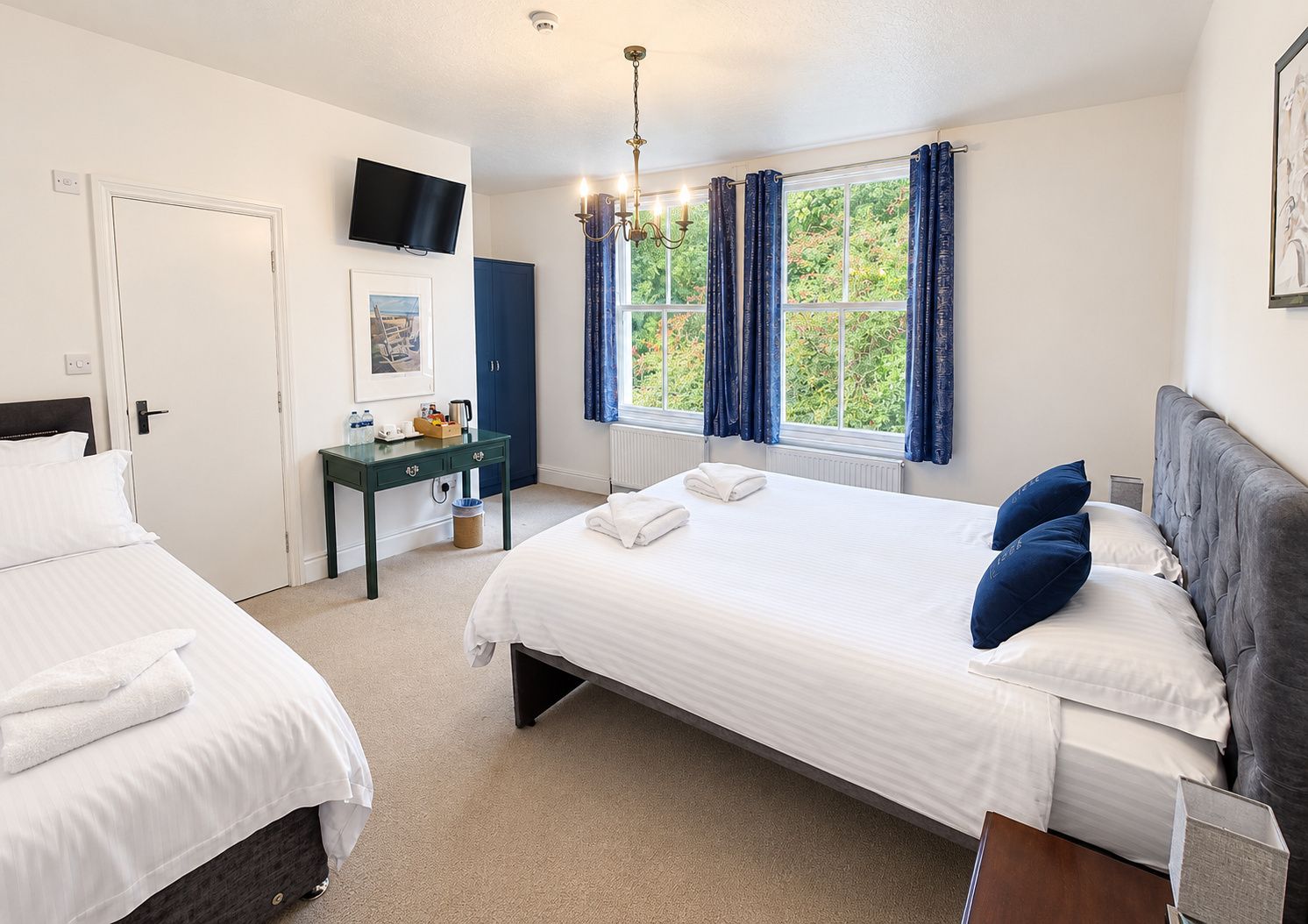 A hotel room with two beds, a desk, a television, and a window with curtains.