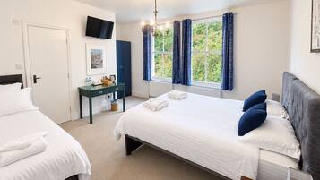 A hotel room with two beds, a desk, a television, and a window with curtains.
