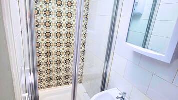 Un baño con ducha, lavamanos y espejo.